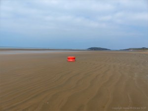 Red buoy washed up on sandy beach as flotsam