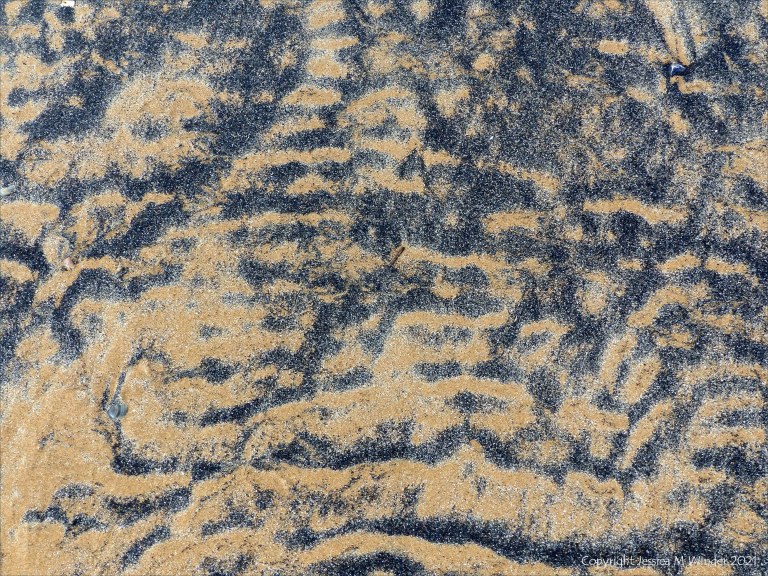 Patterns of black sediment on sand at low tide