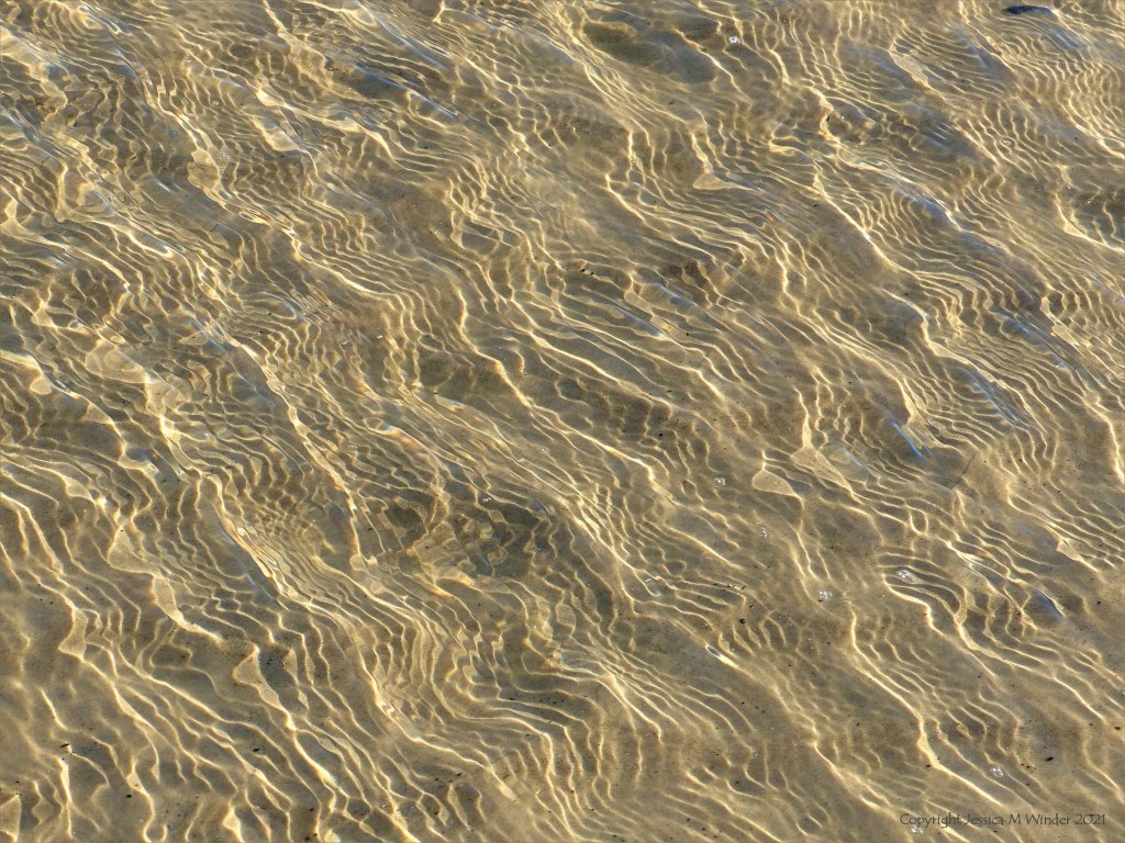 Details of reflected light patterns on sea water washing over sand at the beach