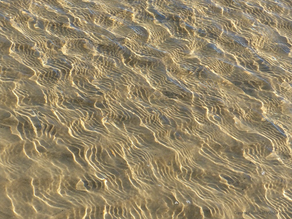 Details of reflected light patterns on sea water washing over sand at the beach