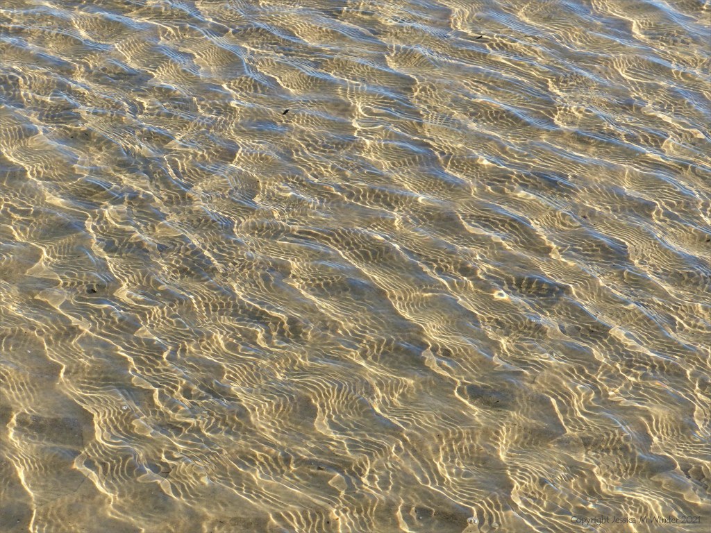 Details of reflected light patterns on sea water washing over sand at the beach
