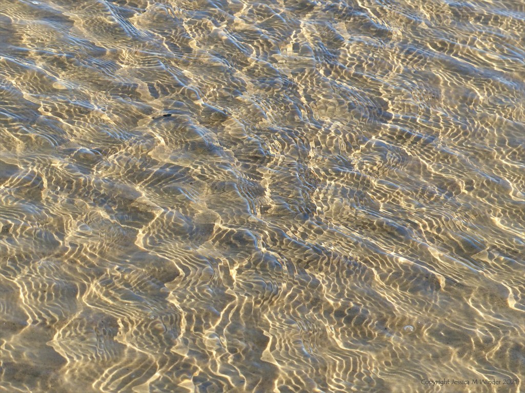 Details of reflected light patterns on sea water washing over sand at the beach