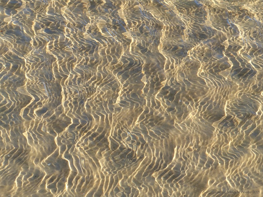 Details of reflected light patterns on sea water washing over sand at the beach