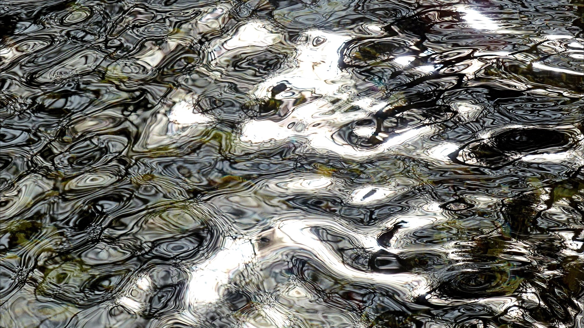 Detail of black and white dappled light reflection patterns on flowing river water