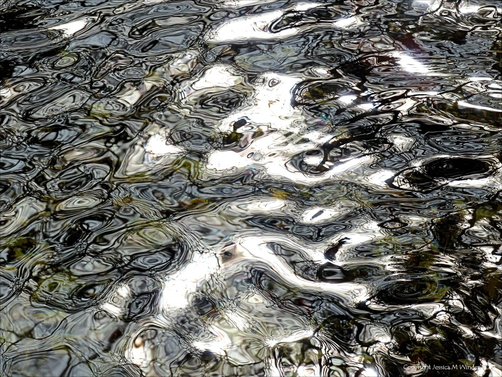 Detail of black and white dappled light reflection patterns on flowing river water