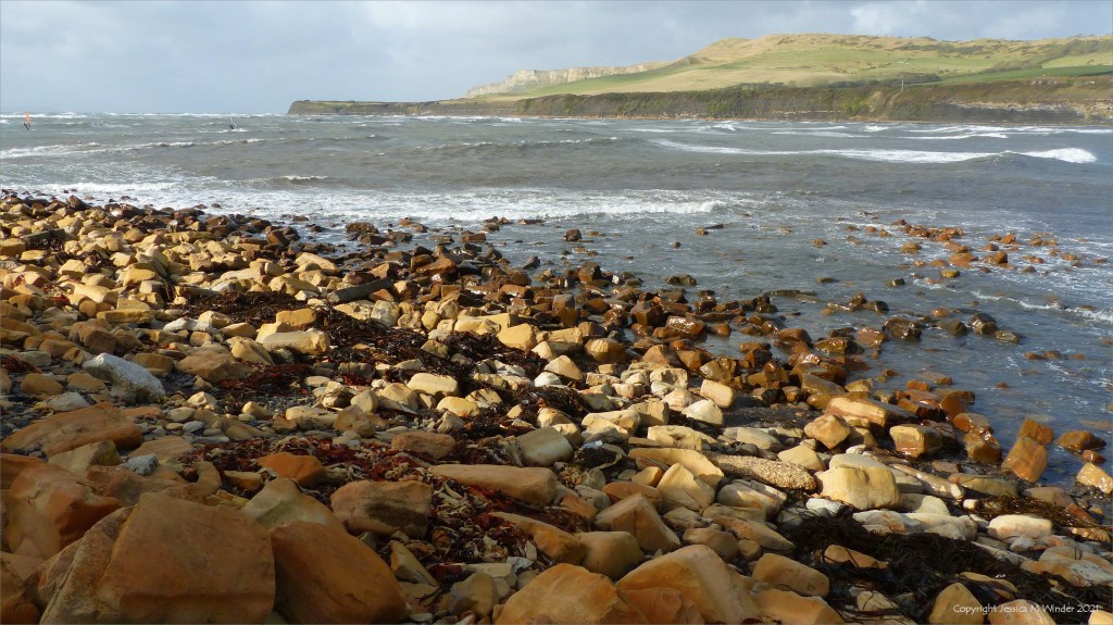 Windy day at Kimmeridge Bay in Dorset 31 October 2021 with boulder shore, cliffs, cloudy sky, and rough sea.