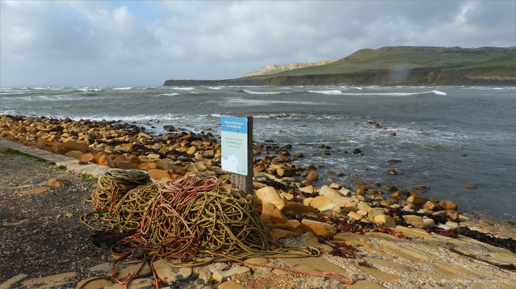 Windy day at Kimmeridge Bay in Dorset 31 October 2021 with pile of rope, boulder shore,cliffs,in the distance, cloudy sky, and rough sea.