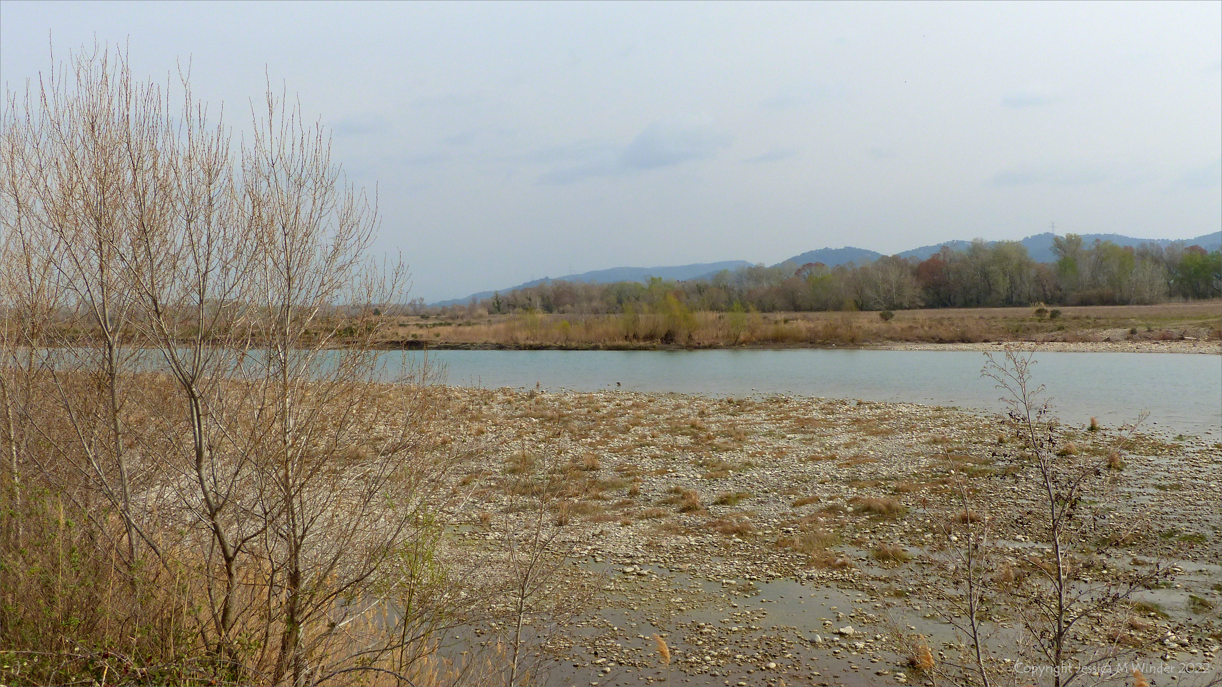 The pebble-lined banks of the Durance River, with trees and hills on the south side, near Lauris in Provence