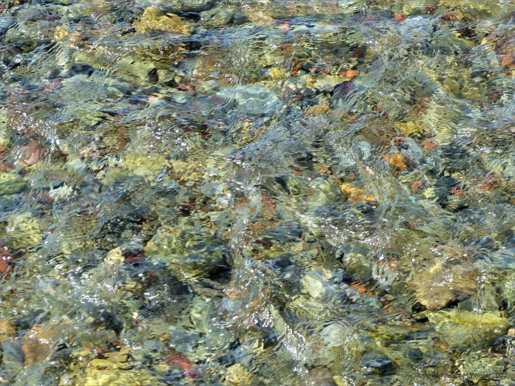 Clear water flowing over coloured pebbles in a beach stream