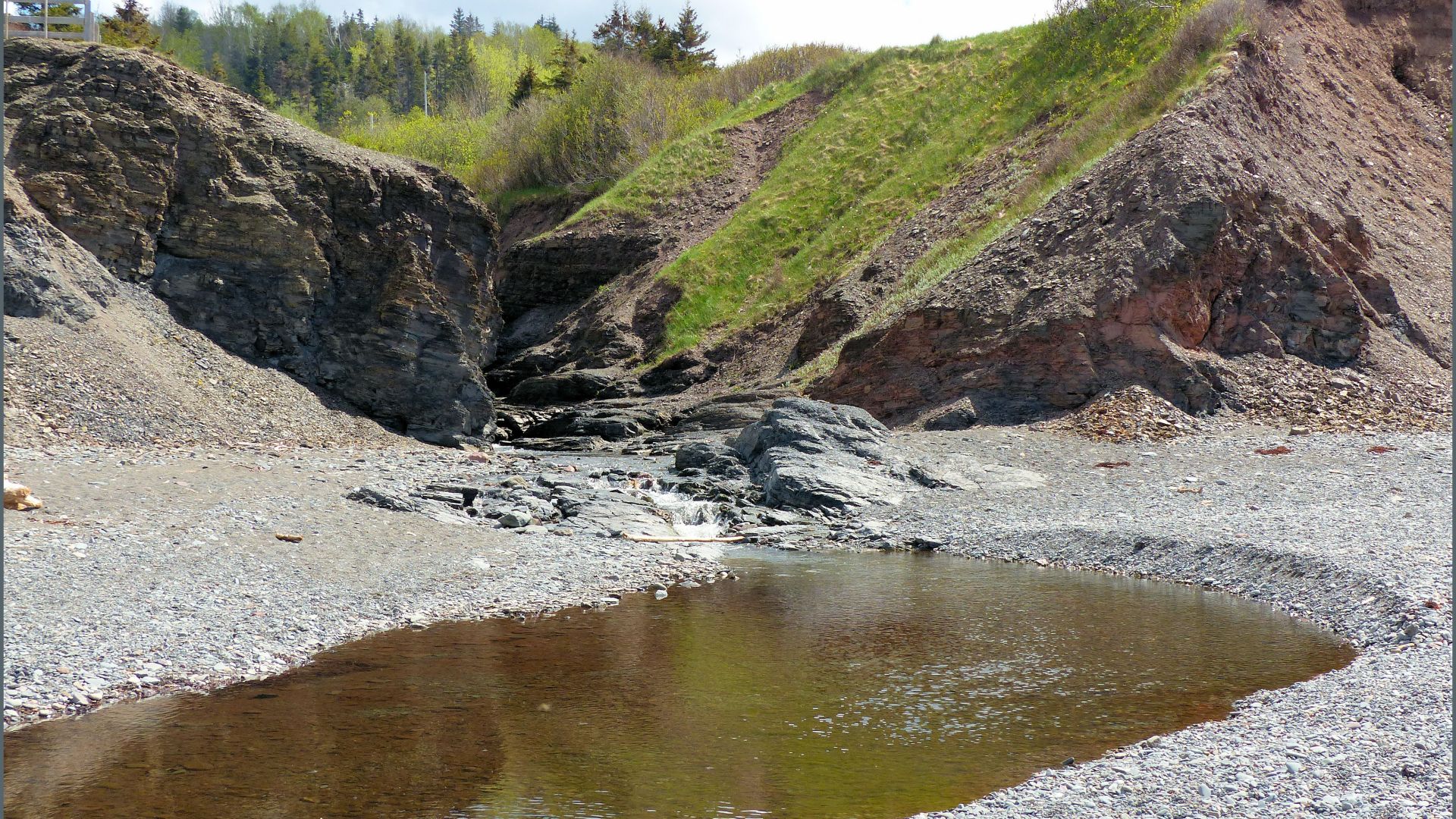 Stream cutting through soft low cliffs by a pebble beach