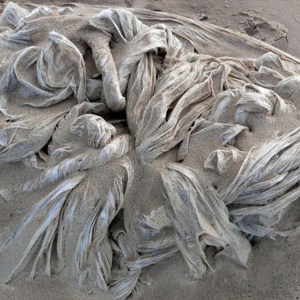 Detail of texture in sand-covered tangled polythene sheeting on the beach
