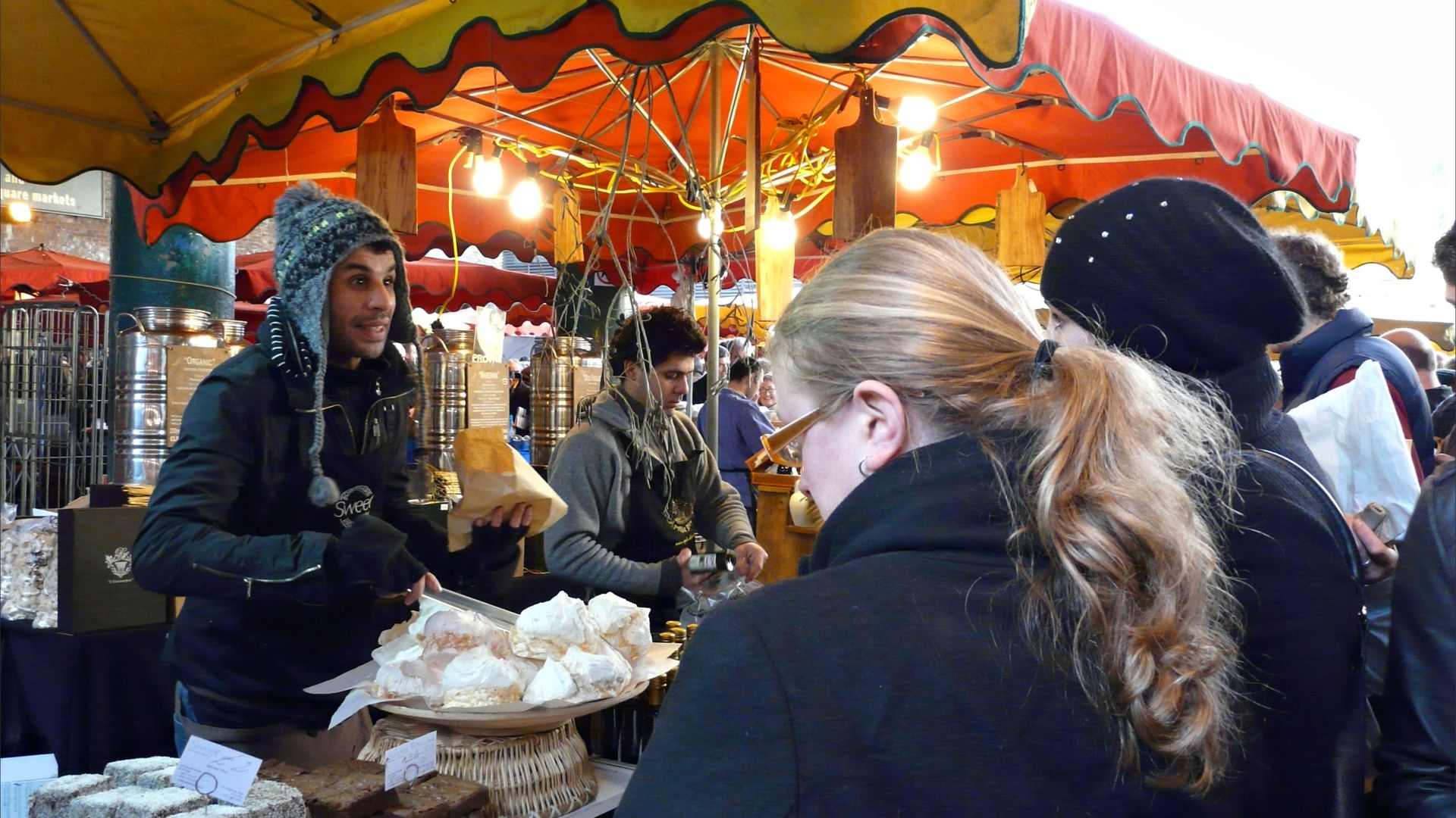 Cake stall in indoor market with people and meringues