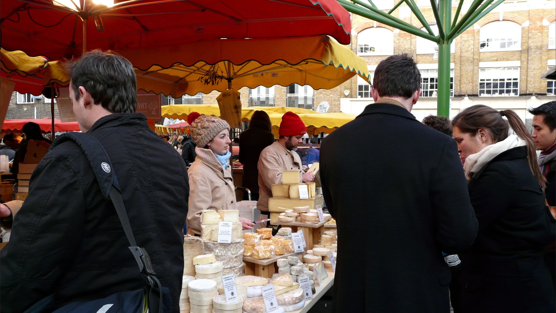 Stallholders selling cheese at the market with customers around the stall