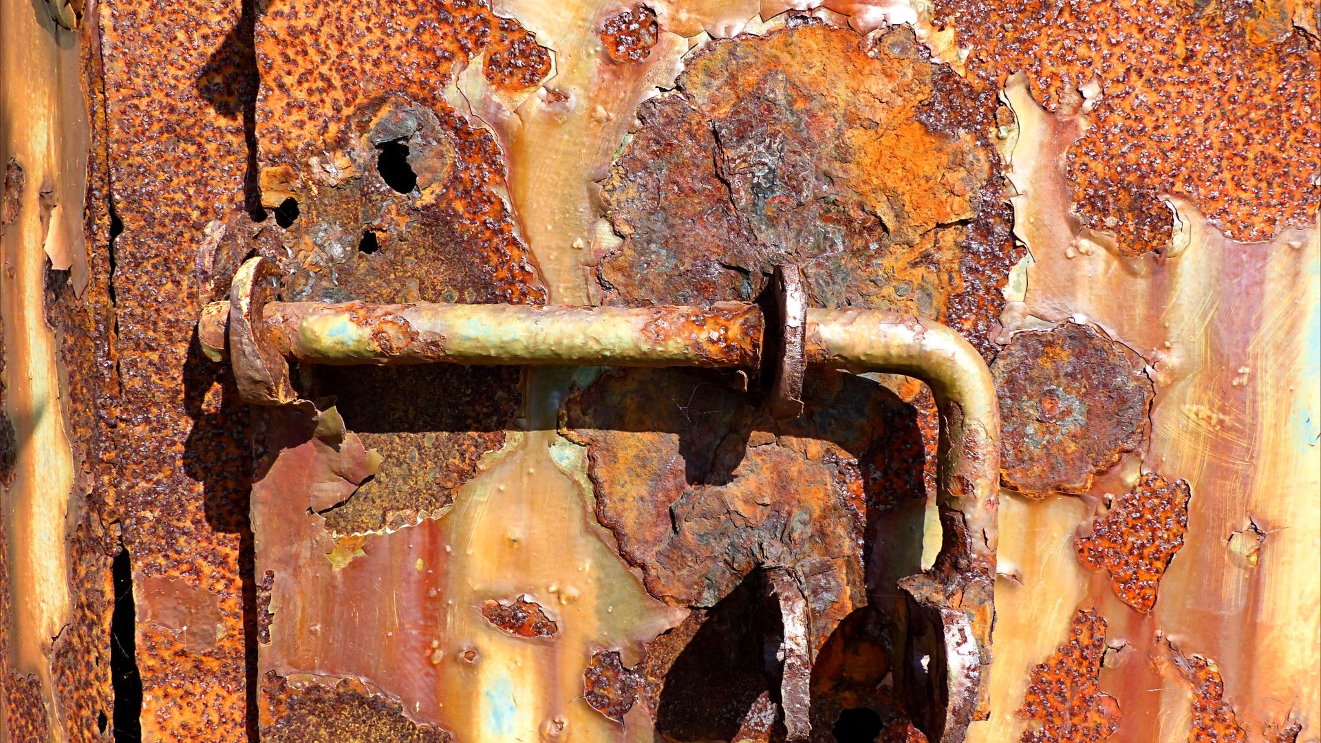 The texture of rusting iron and peeling paint on old bunker door with latch bolt