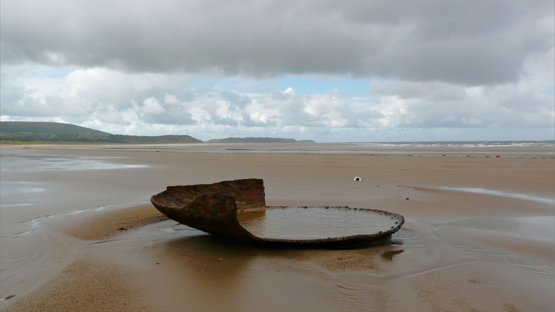 The remains of a large rusting iron dish-like object on a sandy beach