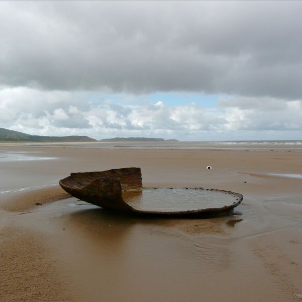 The remains of a large rusting iron dish-like object on a sandy beach