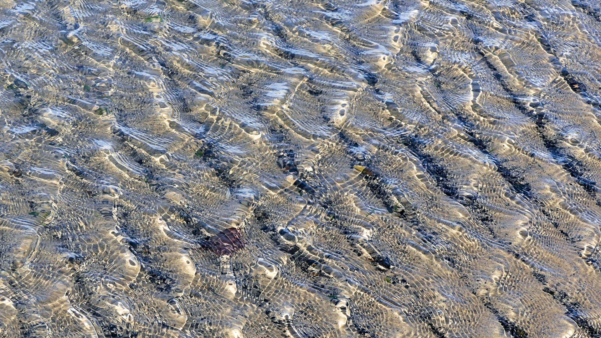 Natural abstract patterns of light reflected on wind-driven ripples in shallow water on the beach at Ogmore-by-Sea on the Glamorgan Heritage Coast in South Wales