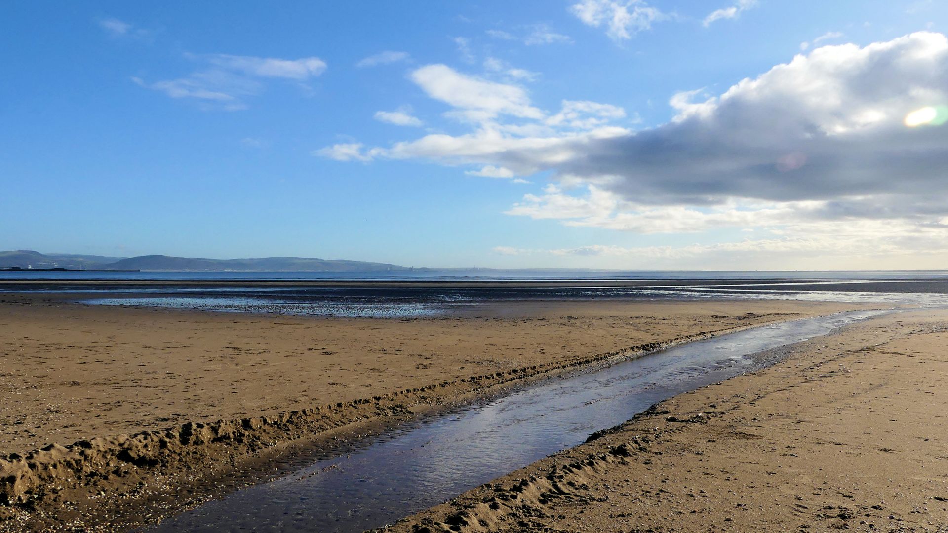Beach stream crossing sand ripples and flowing out into the bay